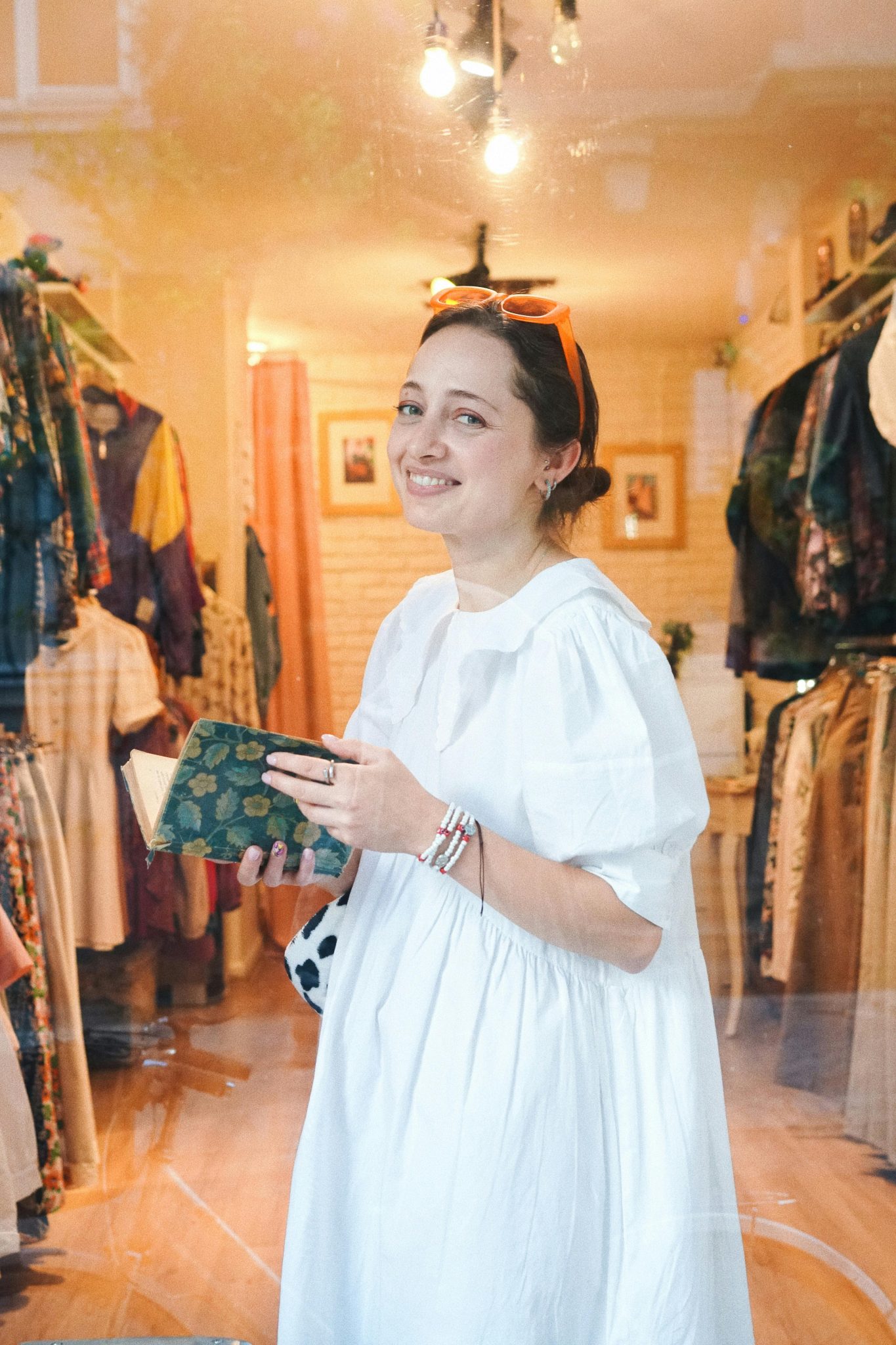 Smiling woman in white dress holding a book inside a fashion boutique.