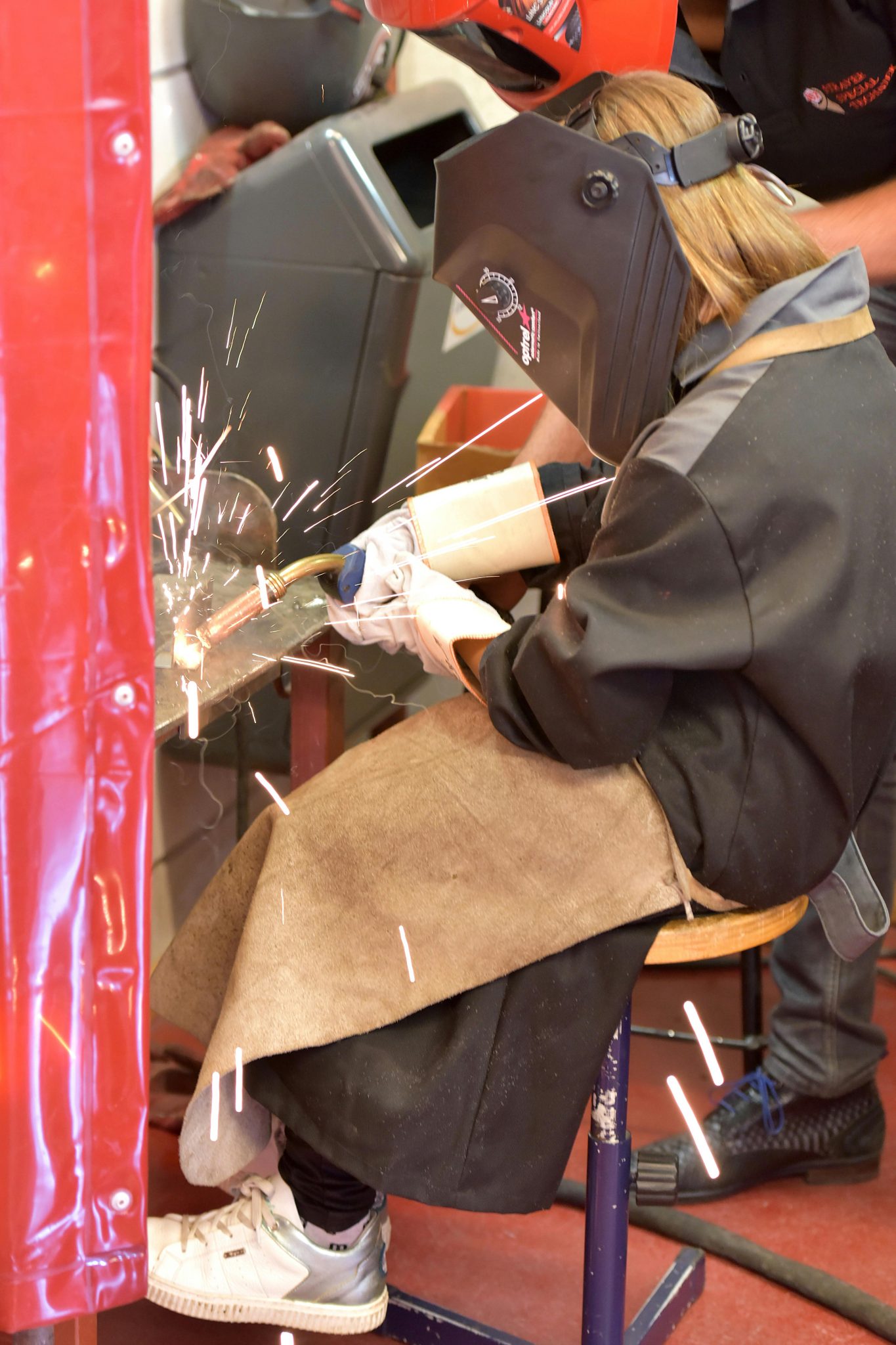 A woman welder works with sparks flying, focused on metalwork in an industrial environment.