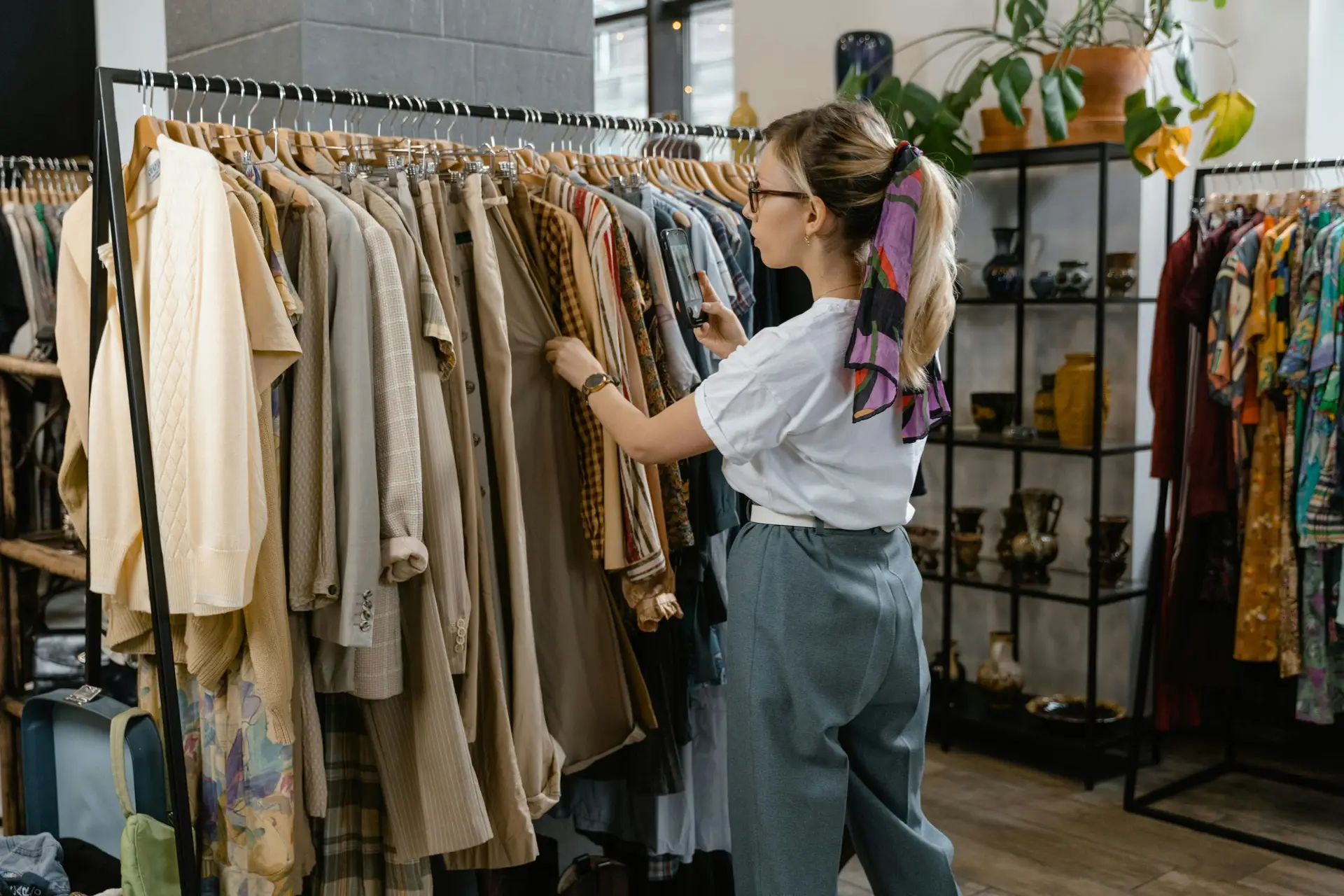 Woman browsing through clothes on hangers in a stylish boutique setting.