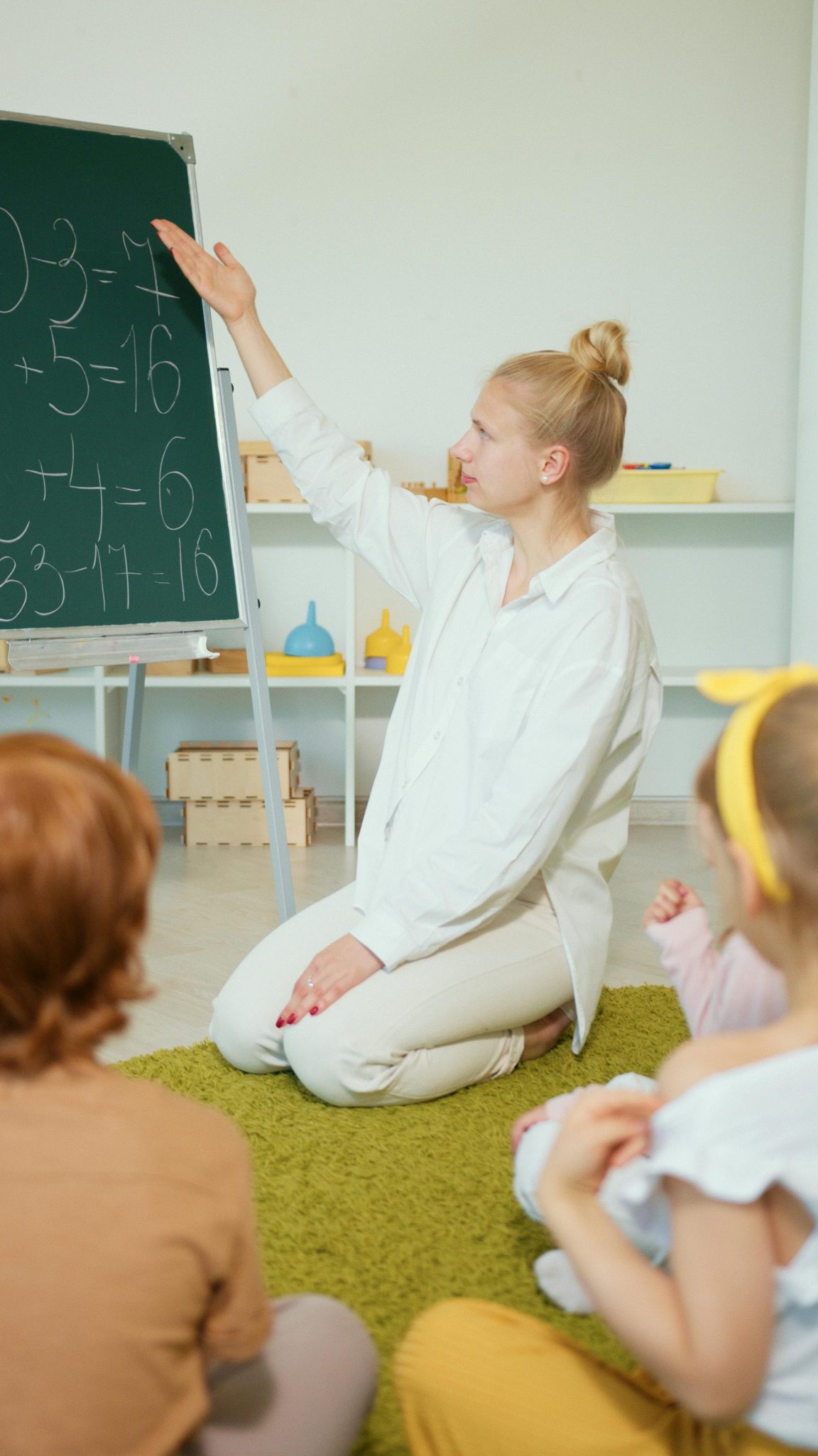 Teacher instructing children with math problems on chalkboard in classroom.