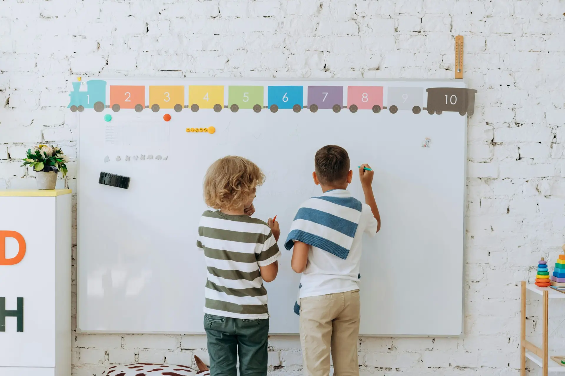 Two boys writing on a colorful classroom whiteboard, enhancing learning.