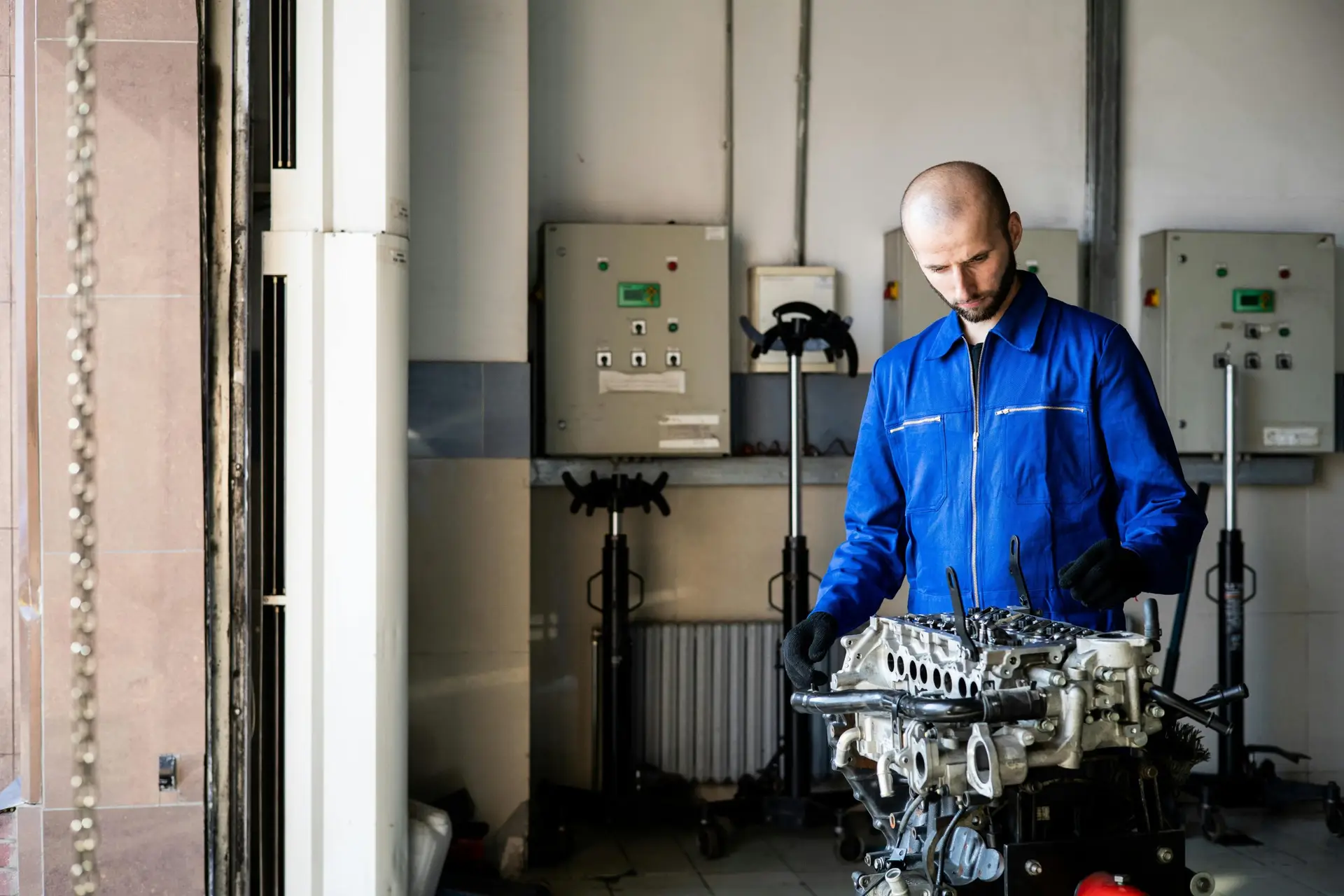 A mechanic in blue coveralls inspects an engine in a repair shop.