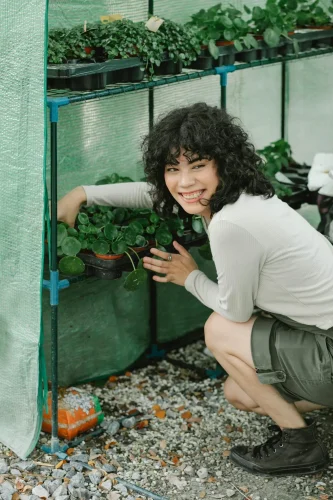 A joyful woman tending to plants in a greenhouse, exuding positivity and nature care.